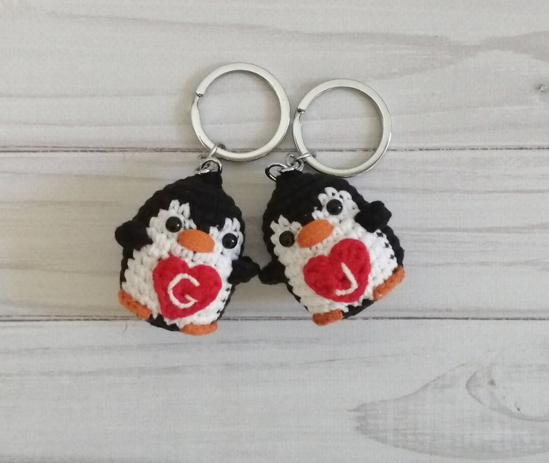 May include: Two crocheted penguin keychains with black and white bodies and red hearts with the letters "G" and "J" on them.
