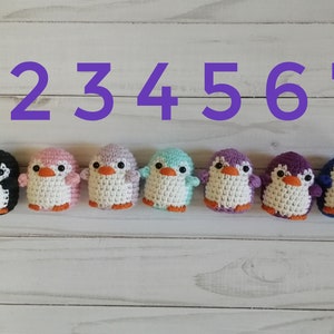 May include: Seven crocheted penguin toys in different colors, numbered 1 through 7. The penguins are black, pink, purple, light blue, lavender, purple, and blue.