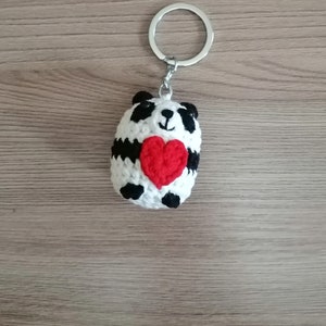 May include: A white crocheted panda bear keychain holding a red heart. The keychain is attached to a silver key ring.