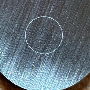 May include: A close-up of a round, silver metal disc with a white circle etched in the center.