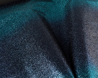 May include: Close-up of a fabric with a gradient of teal and black glitter. The fabric has a textured, sparkly appearance.
