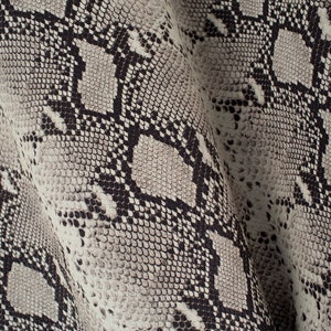 Op de afbeelding: Close-up van een textuurdoek met een slangenhuidpatroon in grijstinten en zwart.