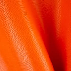 May include: A vibrant orange material featuring a fine, horizontal ribbed texture. The surface is draped in soft, flowing folds that create deep shadows and highlights, emphasising the consistent linear pattern across the entire flexible sheet.