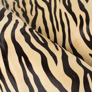 Pode incluir: Close-up de um tecido de estampa de zebra bege e preto. O tecido tem uma textura macia e felpuda.