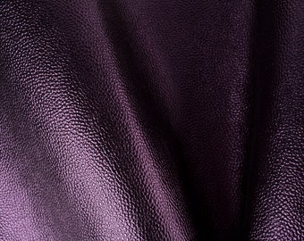 Pode incluir: Close-up de um tecido de couro texturizado roxo escuro com um acabamento macio, liso e ligeiramente brilhante.
