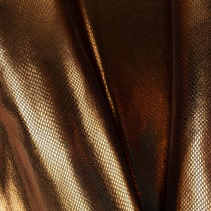 May include: Close-up of a gold fabric with a textured, snake-skin like pattern. The fabric is folded and draped, creating soft, flowing lines.