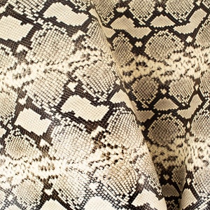 May include: Close-up of a beige and black snakeskin pattern. The pattern is made up of small, overlapping scales.