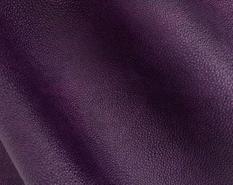 Pode incluir: Close-up de um tecido de couro roxo texturizado. O tecido tem uma superfície granulada e uma cor profunda e rica.