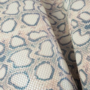 May include: Close-up of a beige and blue snakeskin pattern fabric. The fabric has a textured surface and a repeating pattern of scales.