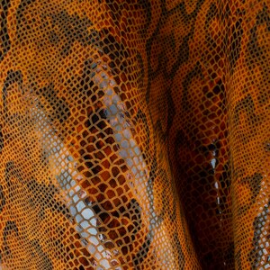 Pode incluir: Close-up de um tecido texturizado com um padrão de pele de cobra em tons de laranja e marrom.