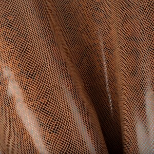 May include: Close-up of a brown snakeskin-textured fabric with a subtle sheen. The fabric is folded and draped, showing the texture and pattern.