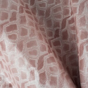 Peut inclure: Gros plan sur un tissu rose avec un motif géométrique blanc. Le tissu a une texture presque écailleuse.