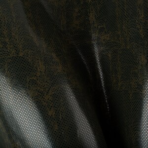 Può includere: Primo piano di un tessuto trasparente marrone scuro con un motivo sottile. Il tessuto ha una trama tessuta ed è leggermente traslucido.