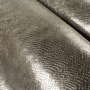 Op de afbeelding: Close-up van een zilveren nep-slangenleer met een textuur, schubbenpatroon.