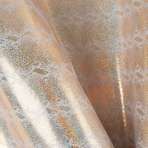 Peut inclure: Gros plan sur un tissu doré iridescent avec un motif de dentelle blanche. Le tissu a une finition chatoyante et scintillante.