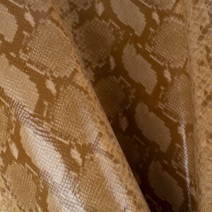 Peut inclure: Gros plan sur un tissu en peau de serpent brun et blanc avec un léger chatoiement. Le tissu a une surface texturée et un motif répétitif.
