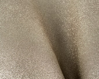 May include: Close-up of a shimmering, textured fabric in a neutral champagne color. The material has a subtle sparkle, with light reflecting off the surface. The fabric is draped, creating soft folds and shadows.