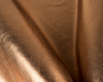 May include: Close-up of a folded piece of metallic copper-colored leather. The leather has a smooth, shiny surface with a subtle texture.