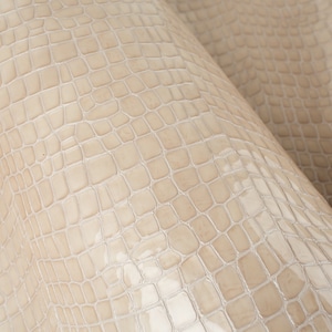 Puede incluir: Primer plano de una tela de cuero beige con relieve de cocodrilo. La textura es detallada y realista.