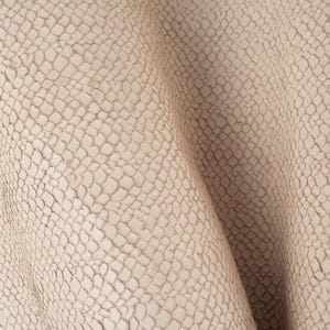 Puede incluir: Primer plano de una tela texturizada de color beige claro con un patrón sutil que se asemeja a escamas. La tela está doblada y tiene una apariencia suave y lisa.