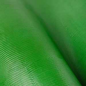 May include: Close-up of a green textured fabric with a subtle sheen. The fabric has a repeating pattern of small, raised squares.