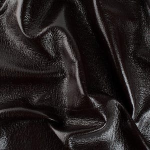 May include: Close-up of a dark brown, glossy leather material. The leather is creased and folded, creating shadows and highlights that emphasize its texture and sheen. The surface appears smooth with subtle variations.