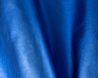 May include: Close-up of a smooth, blue leather fabric with a subtle sheen. The fabric is folded and draped, showcasing its texture and color.