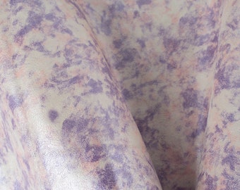 Puede incluir: Primer plano de un material texturizado con un patrón veteado. La tela presenta una mezcla de colores, incluyendo lavanda, rosa pálido y blanco roto, creando una apariencia suave y mezclada. El material está doblado, mostrando su textura.