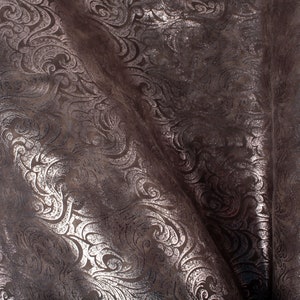 May include: A close-up of a brown fabric with a silver metallic embossed pattern. The fabric has a soft, textured surface and a subtle sheen.