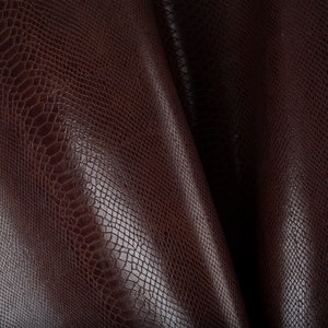 Puede incluir: Primer plano de una tela de imitación de cuero marrón con un patrón texturizado de piel de serpiente.