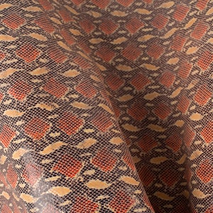 May include: Close-up of a textured fabric with a snakeskin pattern. The fabric is a dark brown color with a light brown and orange pattern.