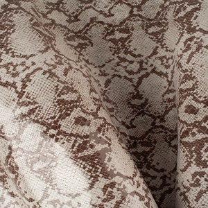 May include: Close-up of a brown and white snakeskin pattern fabric. The fabric has a textured surface and a glossy finish.