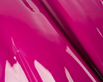 Pode incluir: Close-up de um tecido magenta vibrante com um acabamento brilhante e lustroso. O tecido está dobrado, criando curvas suaves e fluidas.
