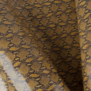 May include: Close-up of a brown and gold fabric with a snakeskin pattern.