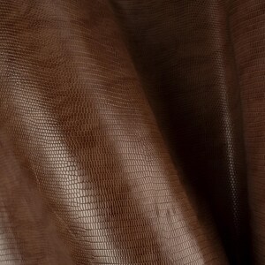 May include: Close-up of a brown leather fabric with a textured, snake-like pattern.