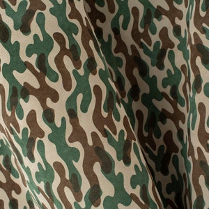 May include: Camouflage fabric with a repeating pattern of organic shapes in shades of green, brown, and beige. The fabric is draped, showing the texture and flow of the material. Ideal for apparel or home decor.