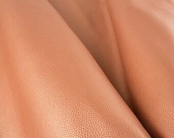 May include: Close-up of a textured, peach-colored leather fabric. The fabric has a subtle sheen and a slightly grainy texture.