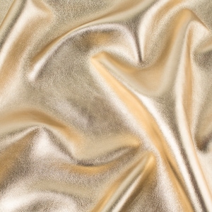 May include: A close-up of a smooth, gold fabric with soft folds and wrinkles. The fabric has a subtle sheen and a luxurious feel.