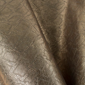 May include: Close-up of a gold fabric with a snakeskin pattern. The fabric has a subtle sheen and a textured surface.