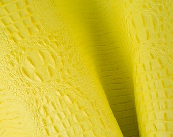 Peut inclure: Gros plan sur un tissu en cuir synthétique jaune embossé crocodile. Le tissu a un motif texturé et écailleux.