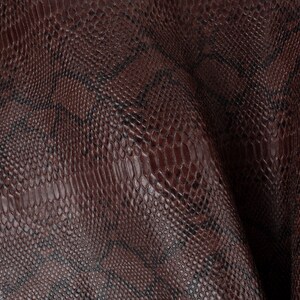 May include: Close-up of a brown snakeskin-textured fabric. The fabric has a subtle sheen and a slightly raised pattern.