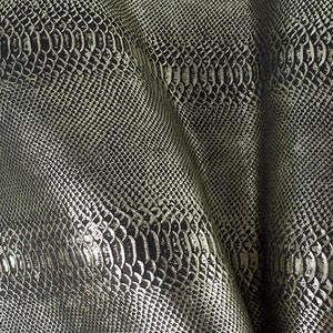 May include: Close-up of a silver snakeskin fabric with a textured pattern. The fabric is folded and has a slight sheen.