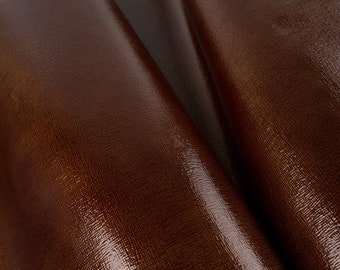 May include: Close-up of a brown leather material with a textured, pebbled surface. The leather has a glossy finish.