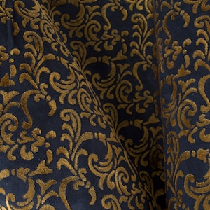 May include: Close-up of a dark blue fabric with a gold damask pattern. The fabric is soft and luxurious, with a subtle sheen.
