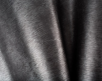 Peut inclure: Gros plan sur un tissu gris foncé texturé avec un motif linéaire subtil. Le matériau a une qualité légèrement réfléchissante, avec des reflets et des ombres créant de la profondeur. Le tissu semble drapé, avec des plis souples.