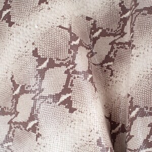 May include: Close-up of a beige fabric with a brown snakeskin pattern.