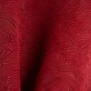 Puede incluir: Primer plano de una tela roja oscura con un patrón texturizado y arremolinado. El diseño presenta una serie de líneas curvas que crean una sensación de movimiento y profundidad. La tela parece suave y lujosa, adecuada para tapicería o fines decorativos.