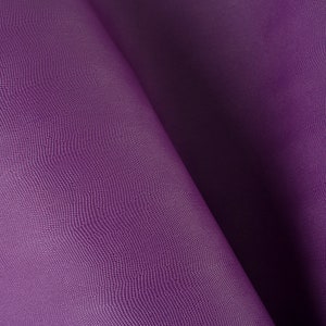 May include: Close-up of a purple fabric with a textured surface. The fabric is folded in half, creating a soft, flowing drape.