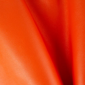 Op de afbeelding: Close-up van een feloranje lederen stof met een textuur. De stof is in het midden gevouwen, waardoor een zachte, vloeiende drape ontstaat.