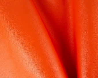 May include: Close-up of a bright orange leather fabric with a textured surface. The fabric is folded in the middle, creating a soft, flowing drape.